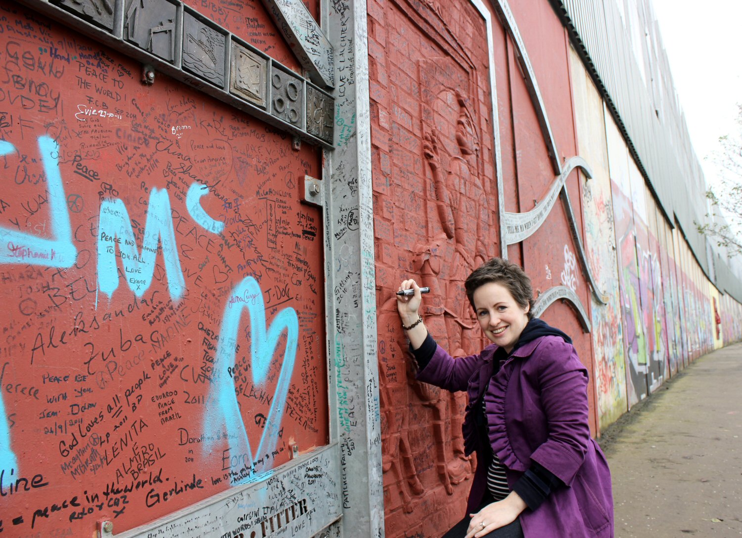 Woman in purple coat holding a pen - preparing to write on the peace wall in Belfast during a Black Cab tour