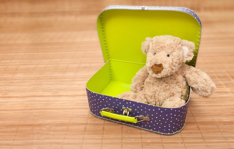 Teddy bear peeks out of a toy suitcase