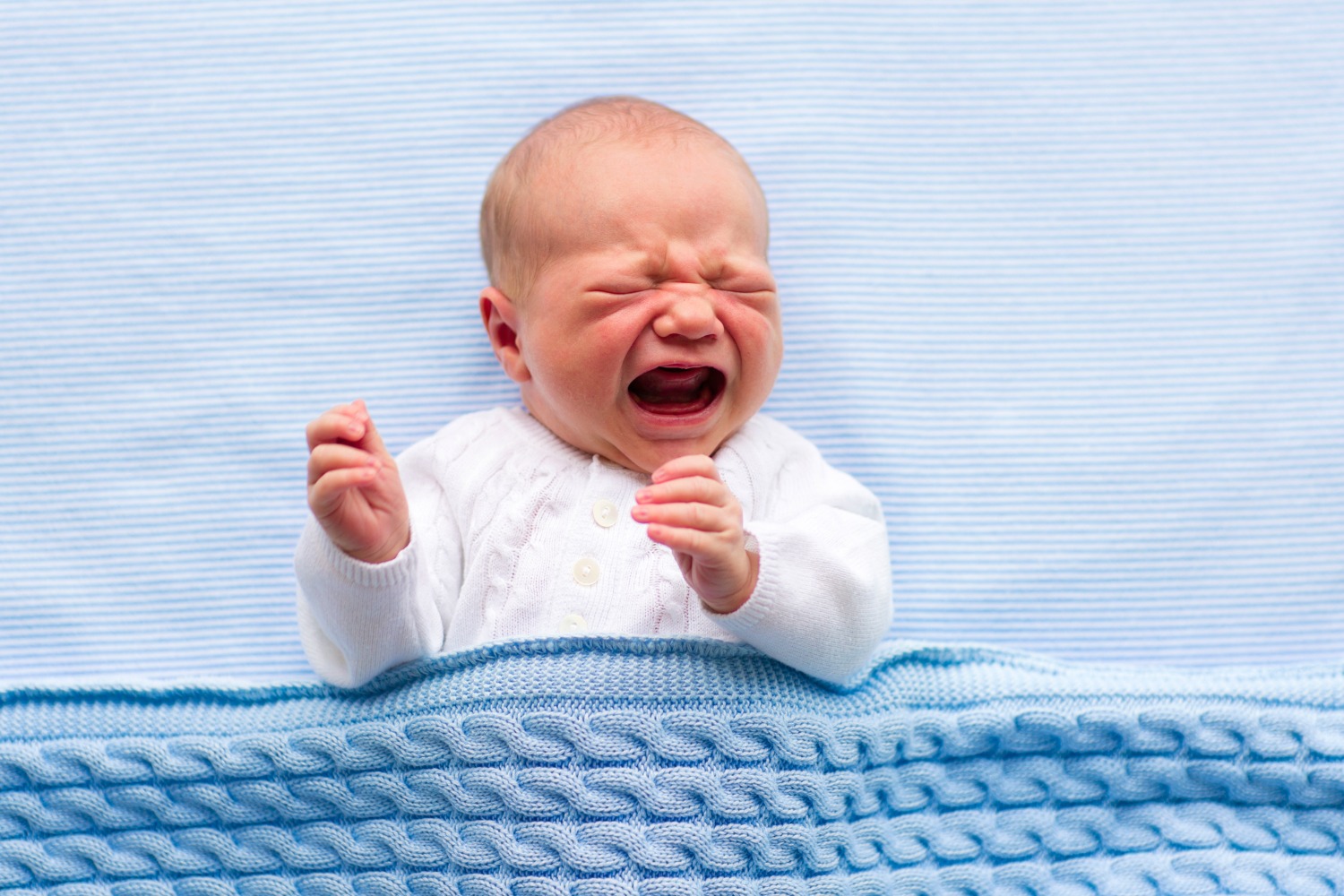 Crying baby in a white babygro under a blue blanket