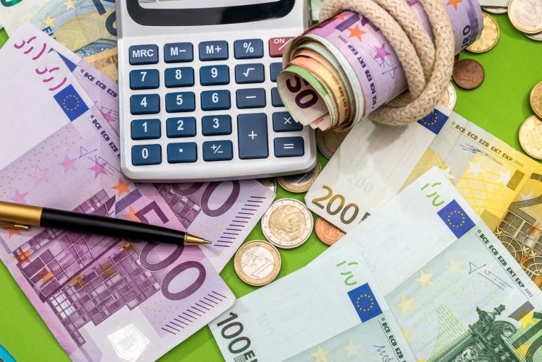 A calculator sitting in a pile of coins and Euro notes - trying to work out the cost of your trip with a holiday budget calculator from Thomas Cook