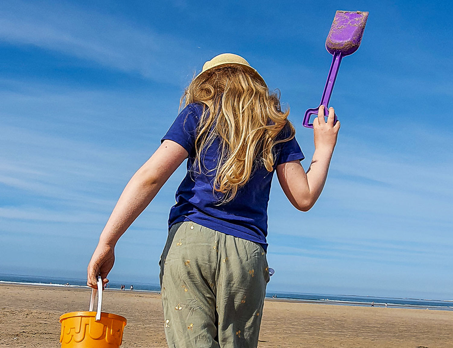 Girl on Bamburgh beach in Northumberland with bucket and spade and sea just visible - my favourite UK family seaside holidays