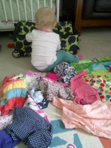 Baby sitting by a suitcase with a pile of clothes