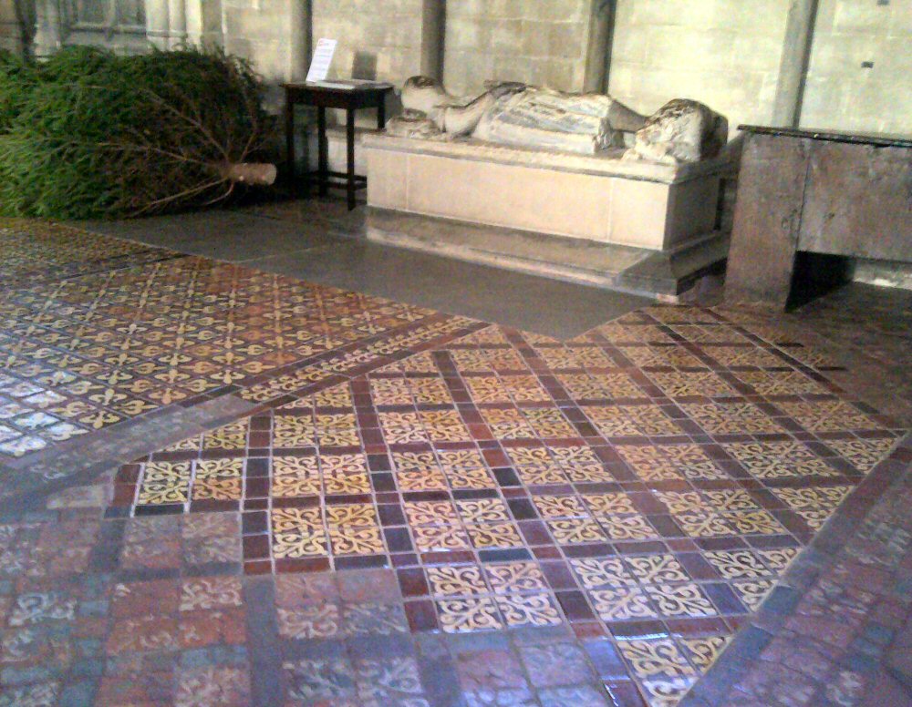 Carved stone tomb seen beyond medieval floor tiles