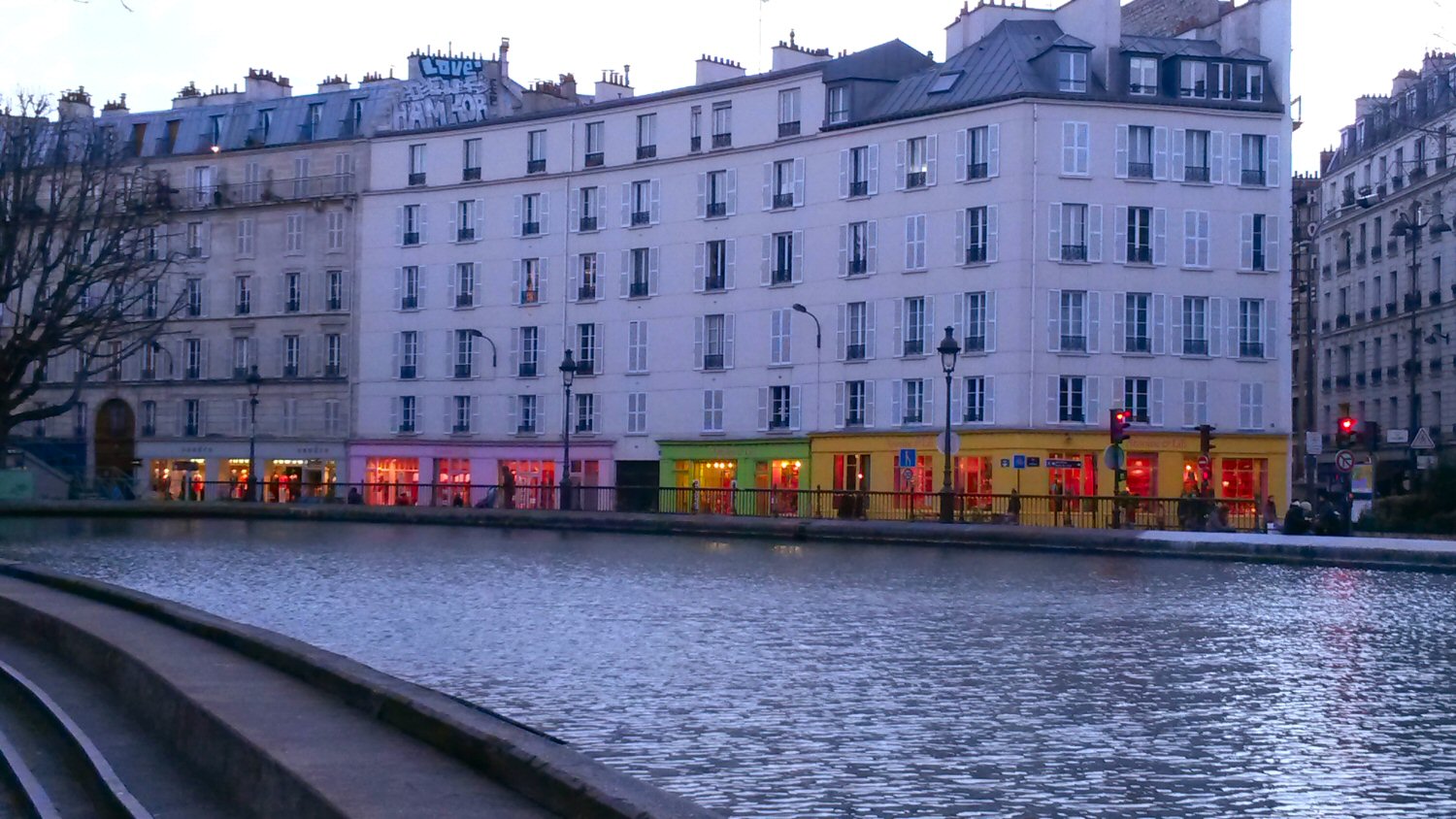 Lit up windows of the brightly coloured boutiques along the waterfront of the Canal St Martin - our AirBNB stay in a flat near Canal Saint Martin in Paris