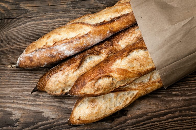 Baguettes in paper bag on wooden background- as well as boulangeries, here are more ideas of where to eat with kids in Paris