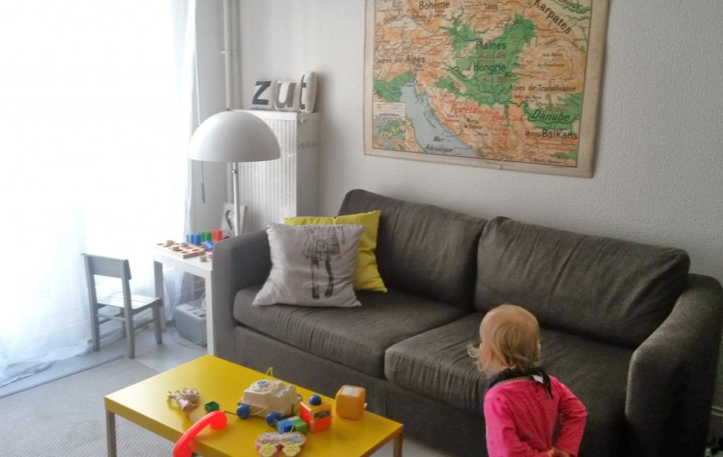 My daughter looks at the toys in the living area of our Paris AirBNB with grey sofa and map on the wall