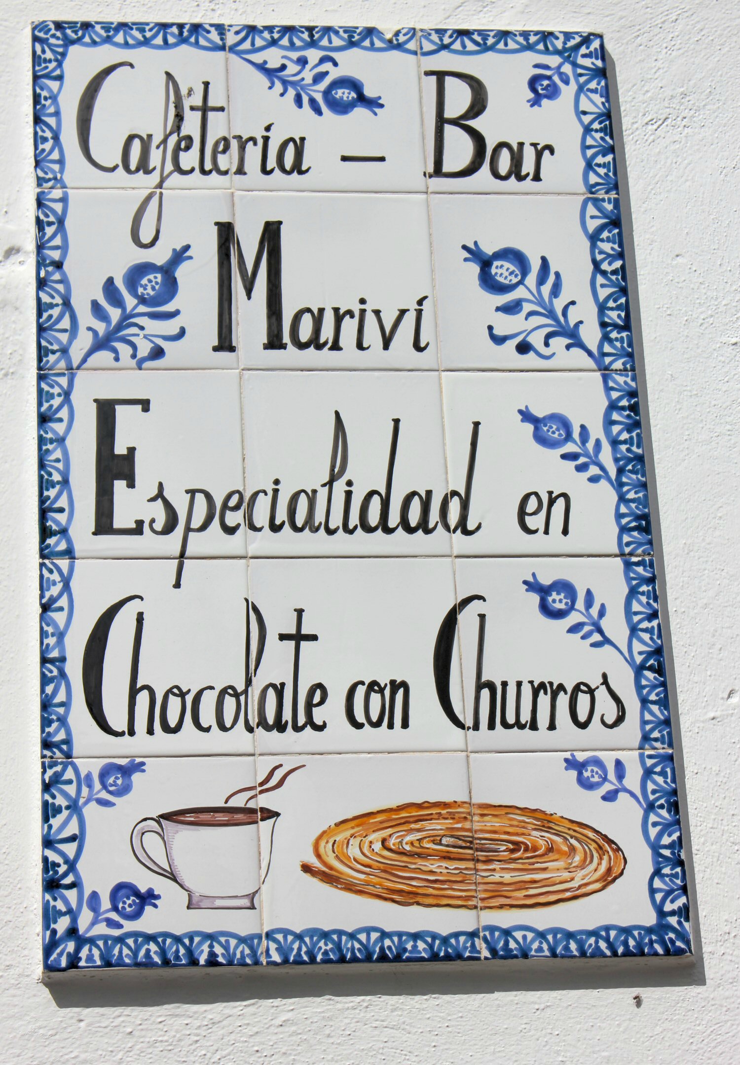 Un cartel con azulejos azules y blancos en una cafetería que muestra churros y chocolate a la venta - mis fotos de Granada