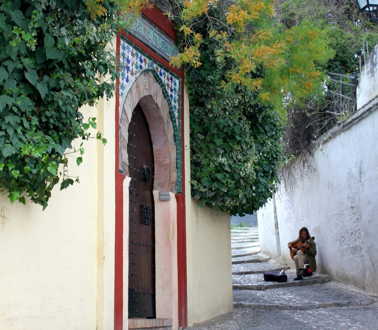 A man sits in one of the white streets of the Albaicin quarter in Granada, playing the guitar - exploring the Albaicin Granada