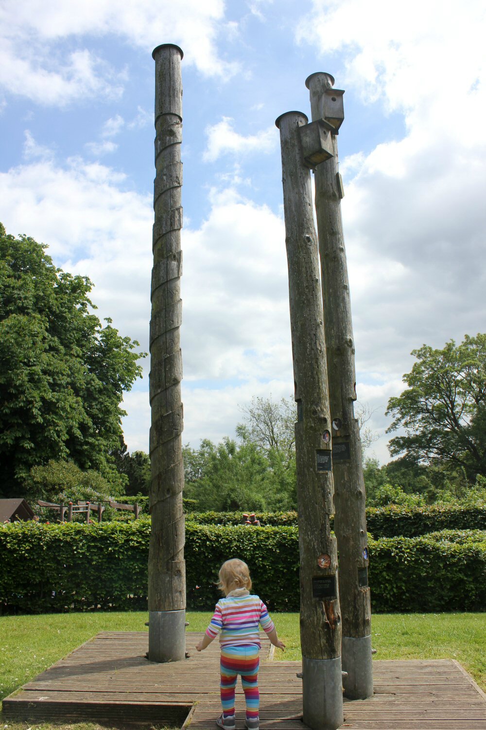 My toddler daughter next to the high carved poles holding bird boxes at Glasgow's botanic gardens