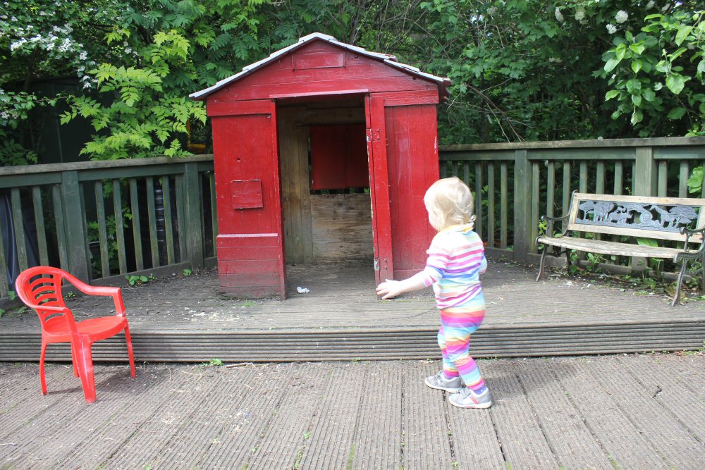 Toddler by the small red wooden house in the children's garden at Glasgow's botanic gardens