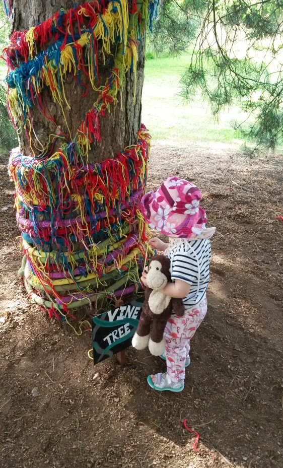 Toddler with monkey next to a tree wrapped in strands of wool, one of the interactive displays at Kew Gardens exhibition Plantasia