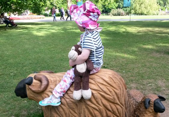 Toddler with toy monkey sitting on a carved wooden sheep - a visit to Kew Gardens and Plantasia