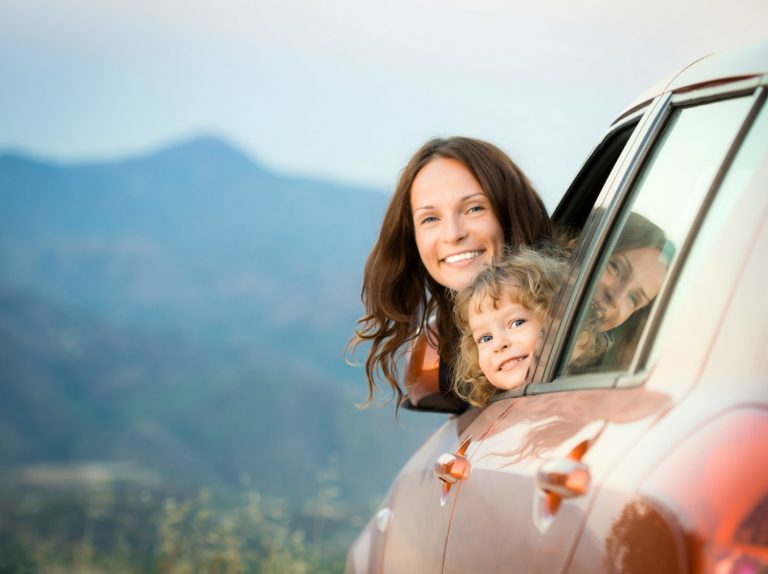 Mother and daughter's head peeking out of a car window with hills in the background - working out how to survive a car journey with a toddler