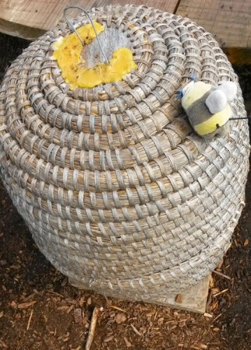 Wicker model of a beehive with a toy bee on the side in the garden at Packwood House
