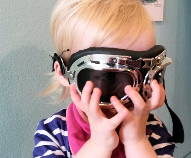 My toddler daughter tries on Mr Toad's goggles in the temporary exhibition - discovering Henley River & Rowing Museum with kids