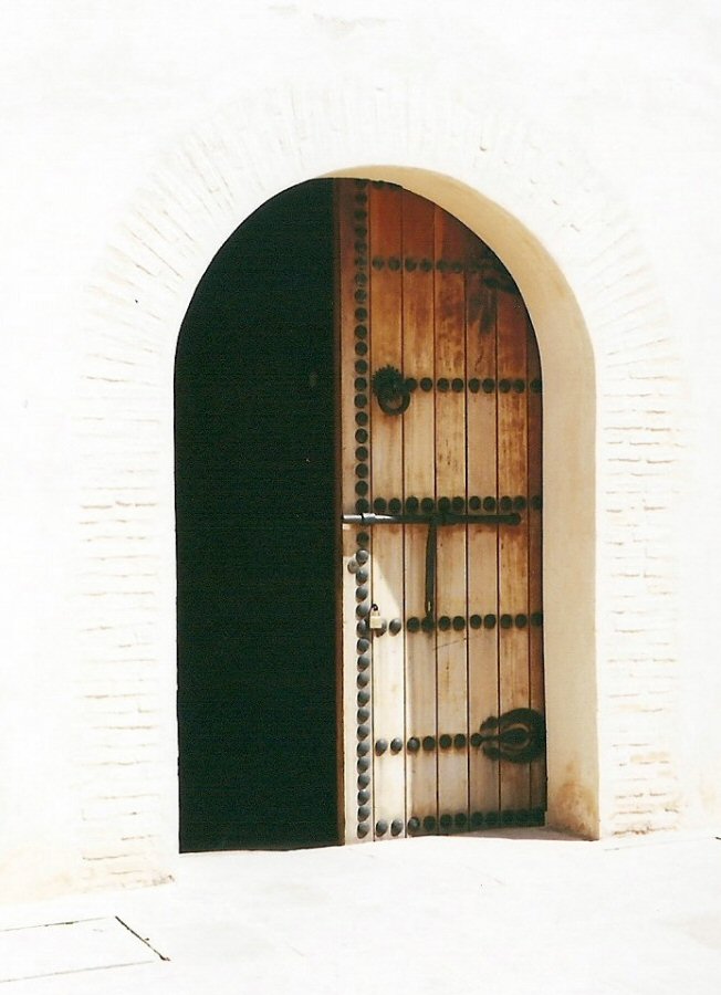 Half open wooden door and shadow in Fes against a blindingly white wall