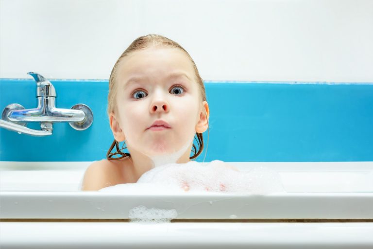 Girl in a bath making a funny face with a bubble beard - adding Munchkin grippy dots to our packing list