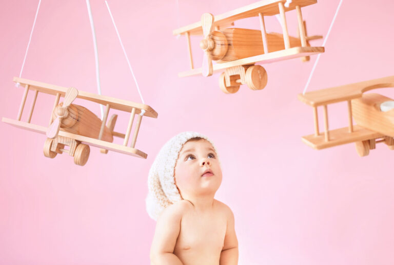 Toddler looking up at wooden planes suspended from the ceiling against a pink background - and my more modern ways to entertain a toddler as you travel