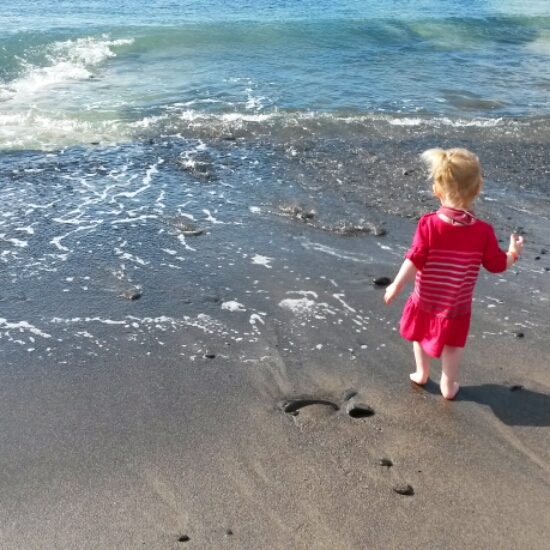 My toddler daughter paddles in the waves by the black sand near Playa Blanca in Lanzarote