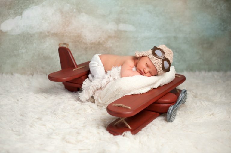 Newborn baby with aviator hat and goggles asleep on a toy plane - my top tips for flying with a baby