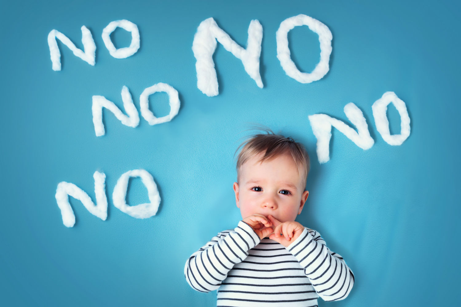 Baby boy on a blue background with the word no repeated in white fluffy shapes - are hotels with adults-only areas best avoided by families