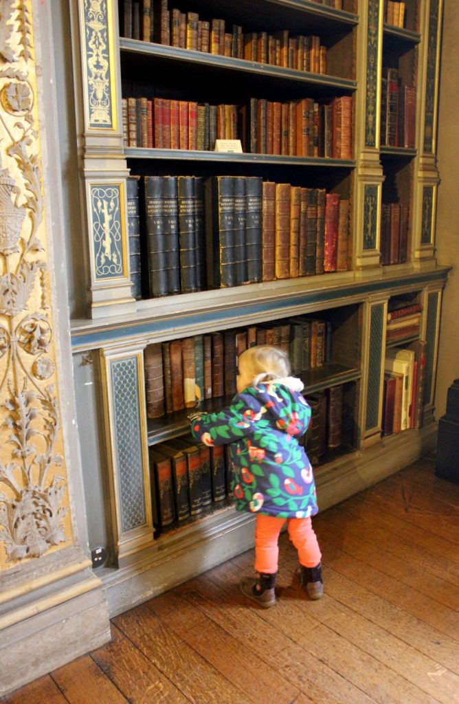 Toddler by the bookcase in the library - visiting Warwick castle with a toddler
