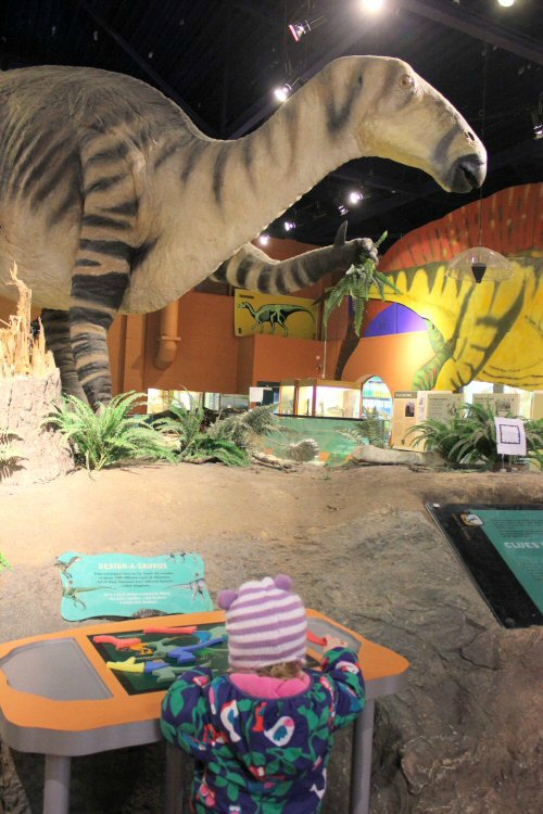 My daughter with one of the interactive exhibits, dwarfed by the dinosaur models around her at Dinosaur Isle