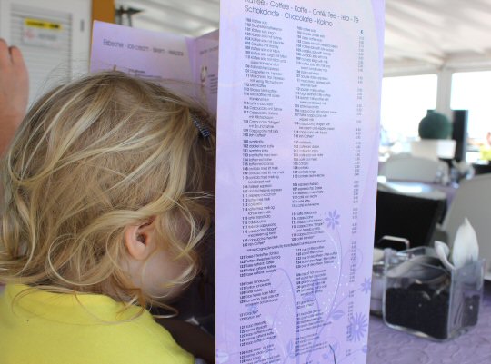My toddler daughter looks inside the huge menu at one of the restaurants on the marina at Puerto de Mogan, Gran Canaria