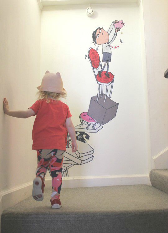 My daughter walks up the stairs at the Lauren Child exhibition at Mottisfont with more illustrations on the walls