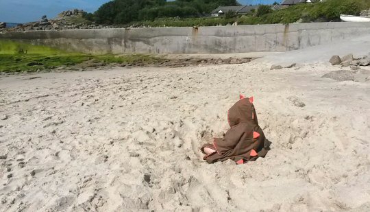 My daughter sits on the beach of St Martin's in the Isles of Scilly wearing a hooded dinosaur towel