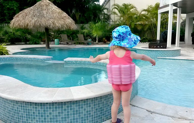 My daughter stands by the side of a swimming pool wearing her Splashabout Floatsuit - my float suit review