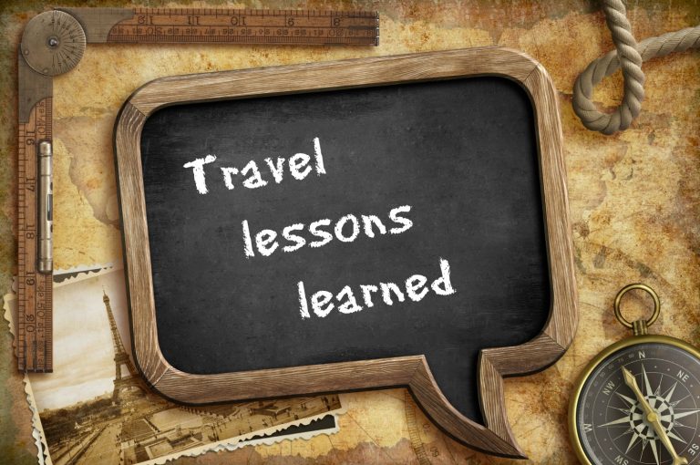 Blackboard showing the words travel lessons learned in chalk writing, against various travel themed objects on a table