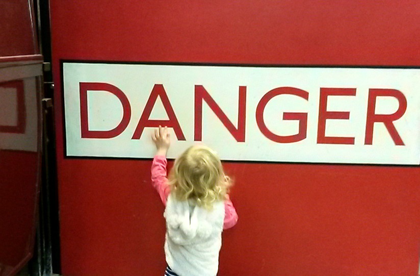 Three year old reaching up to a red danger sign - exploring the London Transport Museum depot with kids