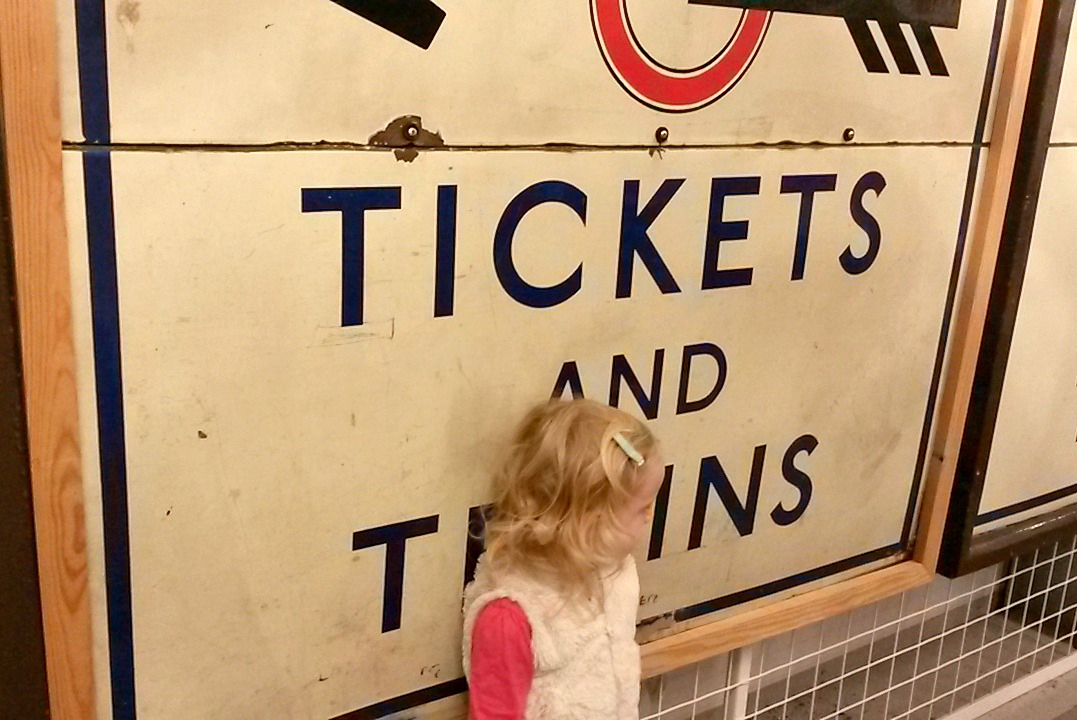 Girl in front of vintage underground sign to tickets and trains - exploring the London Transport Museum depot with kids
