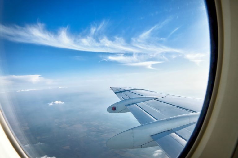 Looking through aircraft window during flight showing a plane wing against a blue sky