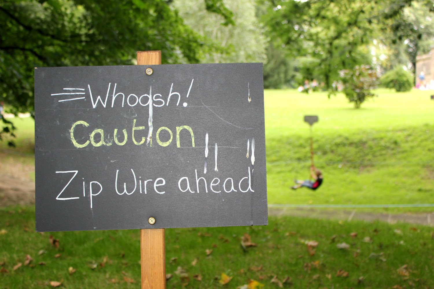 Sign for the zipwire at the Nostell Priory playground as a child zooms past in the background - a weekend break in Yorkshire with kids