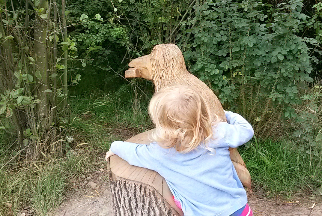 My daughter reaches out to the carved wooden bird - one of the Room on the Broom activities along the Yorkshire trail