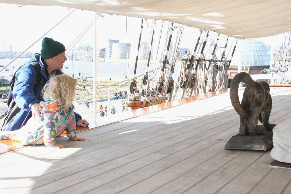My daughter looks at the carved monkey on deck - visiting the Cutty Sark with kids on a day out in Greenwich