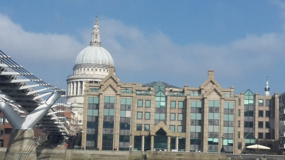 The dome of St Paul's cathedral peeking out behind riverside buildings as seen from a boat on the Thames