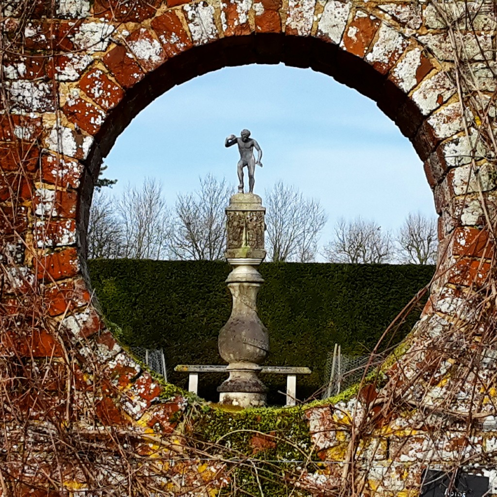 View through a round hole in the wall into a statue in the gardens at Polesden Lacey