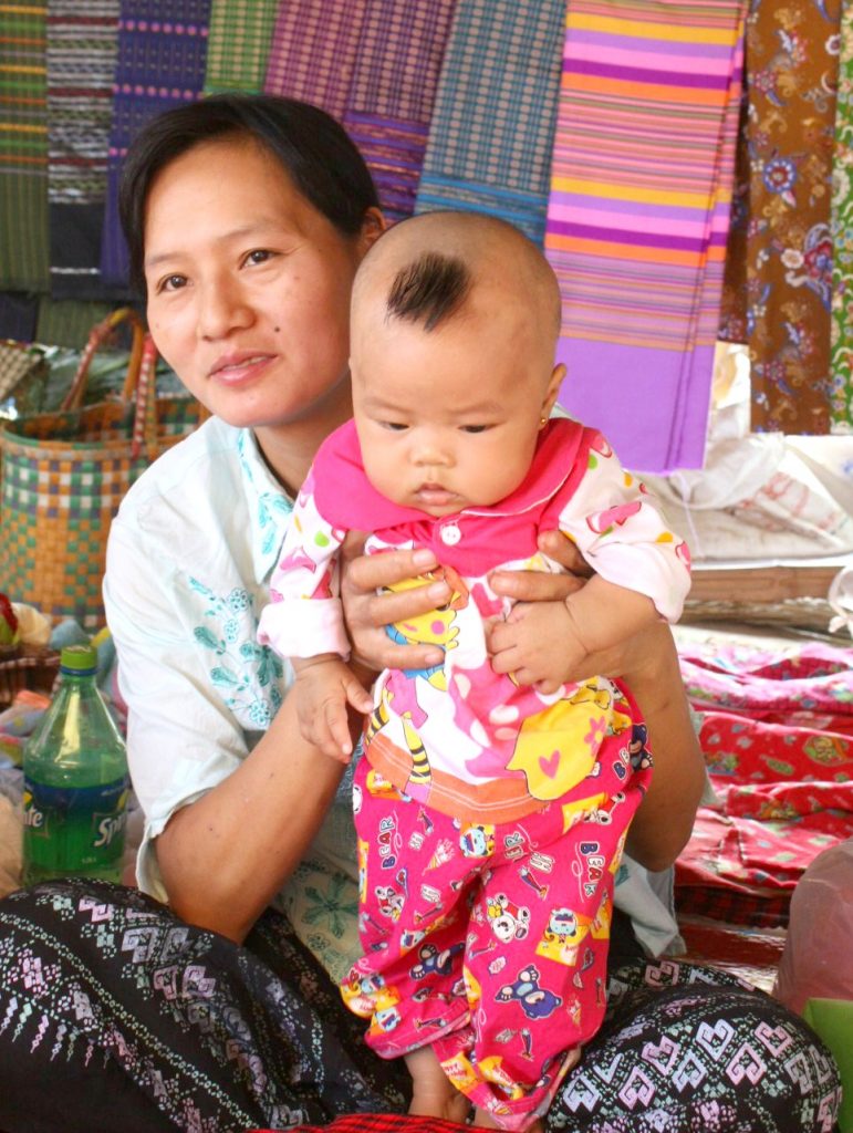 Woman at a market in Burma with her baby. With Burma newly opened up to tourists, and off the beaten track for most families, here are my 12 reasons to visit Burma (Myanmar) - in photos