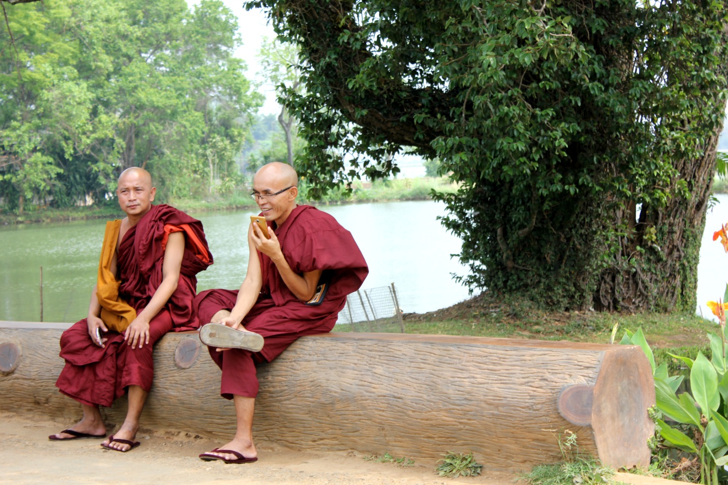 Monks sitting on a log in the gardens at Pyin Oo Lwin, with one talking on his mobile phone - and my Burma travel lessons learned