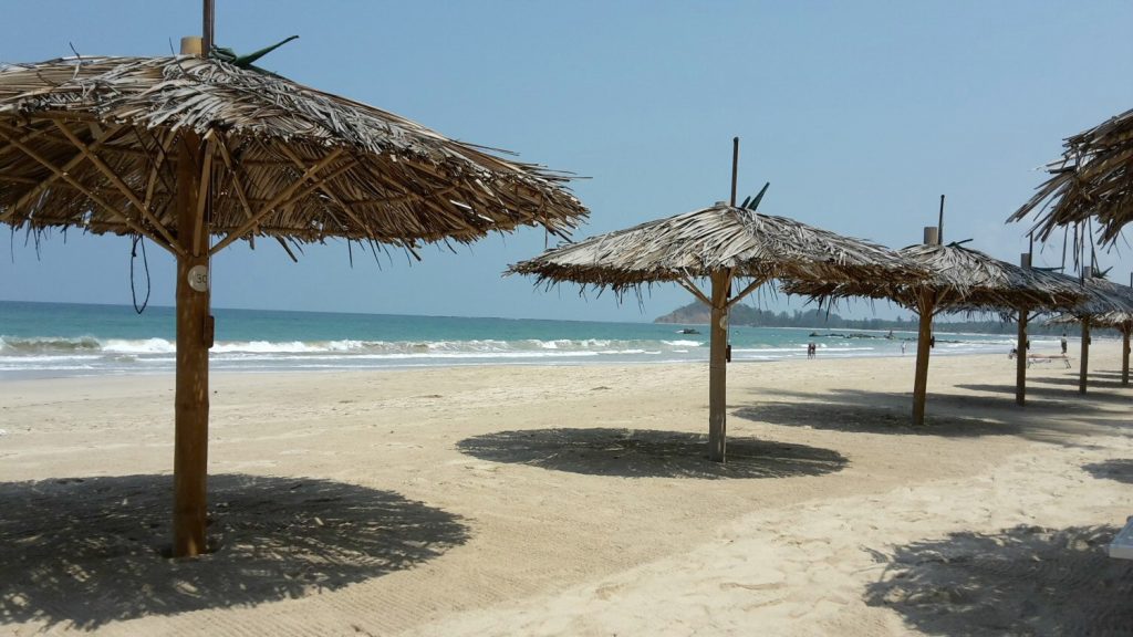 Palm umbrellas cast a shadow on the sand at Ngapali Beach with the Indian Ocean in the background