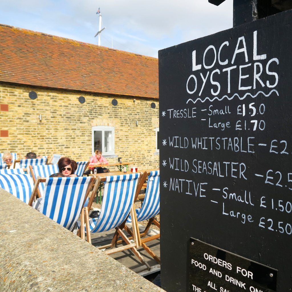 Sign at a restaurant selling local oysters in Whitstable, with prices and blue and white striped deckchairs