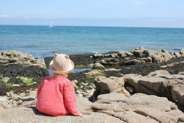 Girl sitting on the rocks at Shoalstone Beach in Devon, one of the best places to go rockpooling in the south west