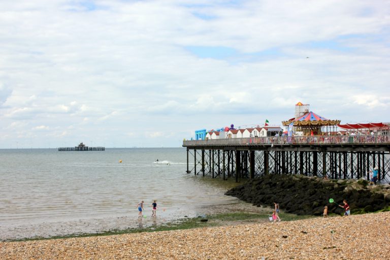The view of the pier at Herne Bay in Kent on a summer day, with the funfair and classic carousel and people paddling