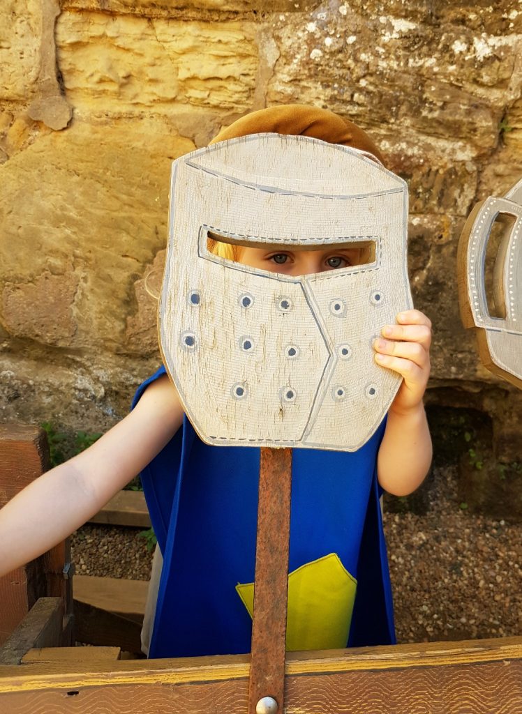 My daughter holding a fake helmet against her face at Bodiam castle, one of the best things to do in East Sussex with kids