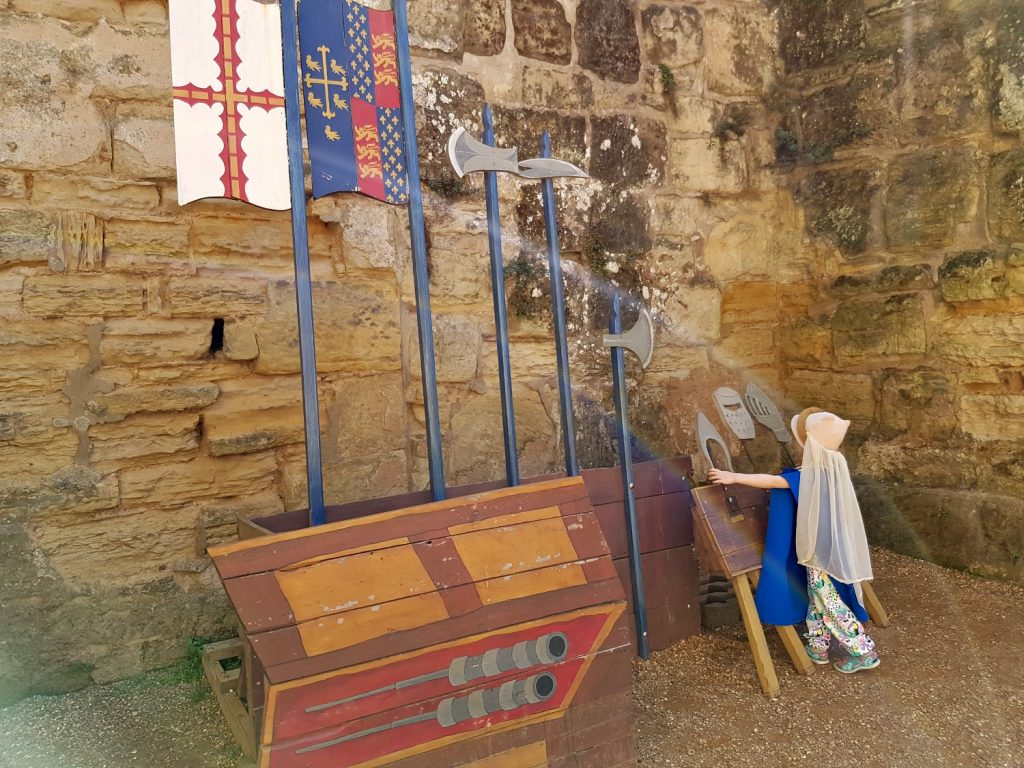 My daughter dressed in some medieval clothes in a room with weapons at Bodiam Castle, one of my top things to do in East Sussex with kids