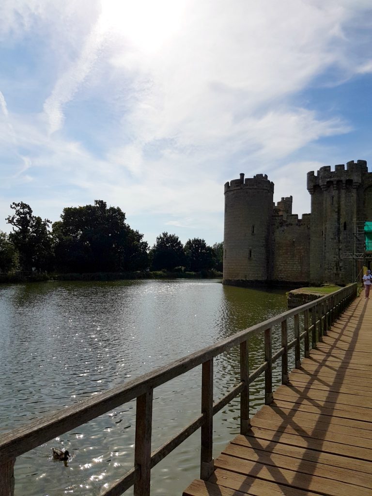 A view of the beautiful Bodiam Castle in East Sussex against blue sky, the medieval towers reflected in the moat - my review and why it's great to visit Bodiam Castle with kids