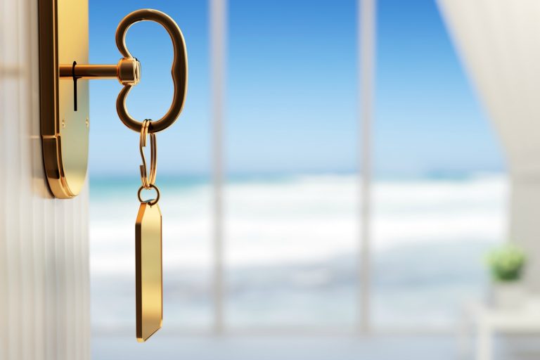 A hotel room key hanging from a door with the sea in the background - how to save money on hotels